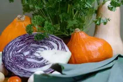 Person preparing fresh vegetables and whole grains in a bright kitchen, with exercise gear and water bottle nearby