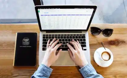 Hands holding a blank notepad over a newsroom desk with laptop and press badges