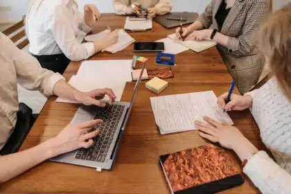 Hands holding a blank notepad over a newsroom desk with laptop and clippings
