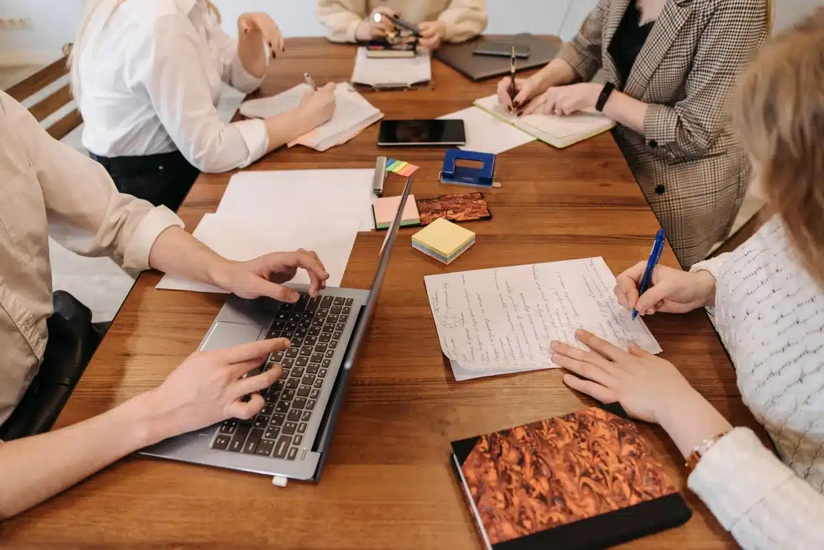 Hands holding a blank notepad over a newsroom desk with laptop and clippings