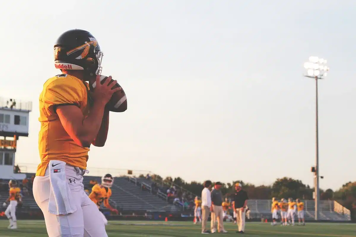 Silhouette of a quarterback on a stadium sideline with goalposts and crowd