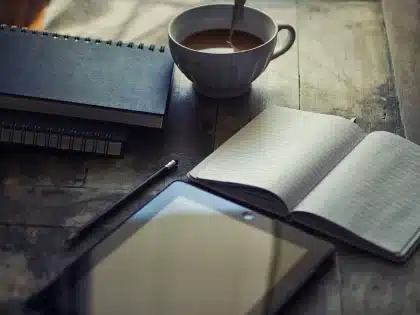 Blank laptop, notebook and coffee on a desk in soft daylight