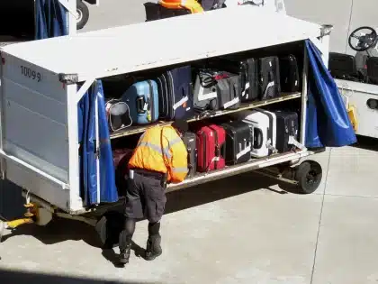 Silhouette of an older delivery worker pushing heavy suitcases across a crowded transport concourse